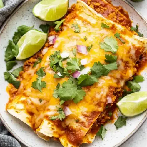 Delicious Ground Beef Enchiladas served with toppings and lime slices.