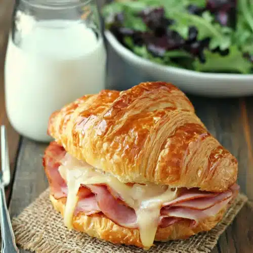Ham and cheese croissant served with salad and milk.