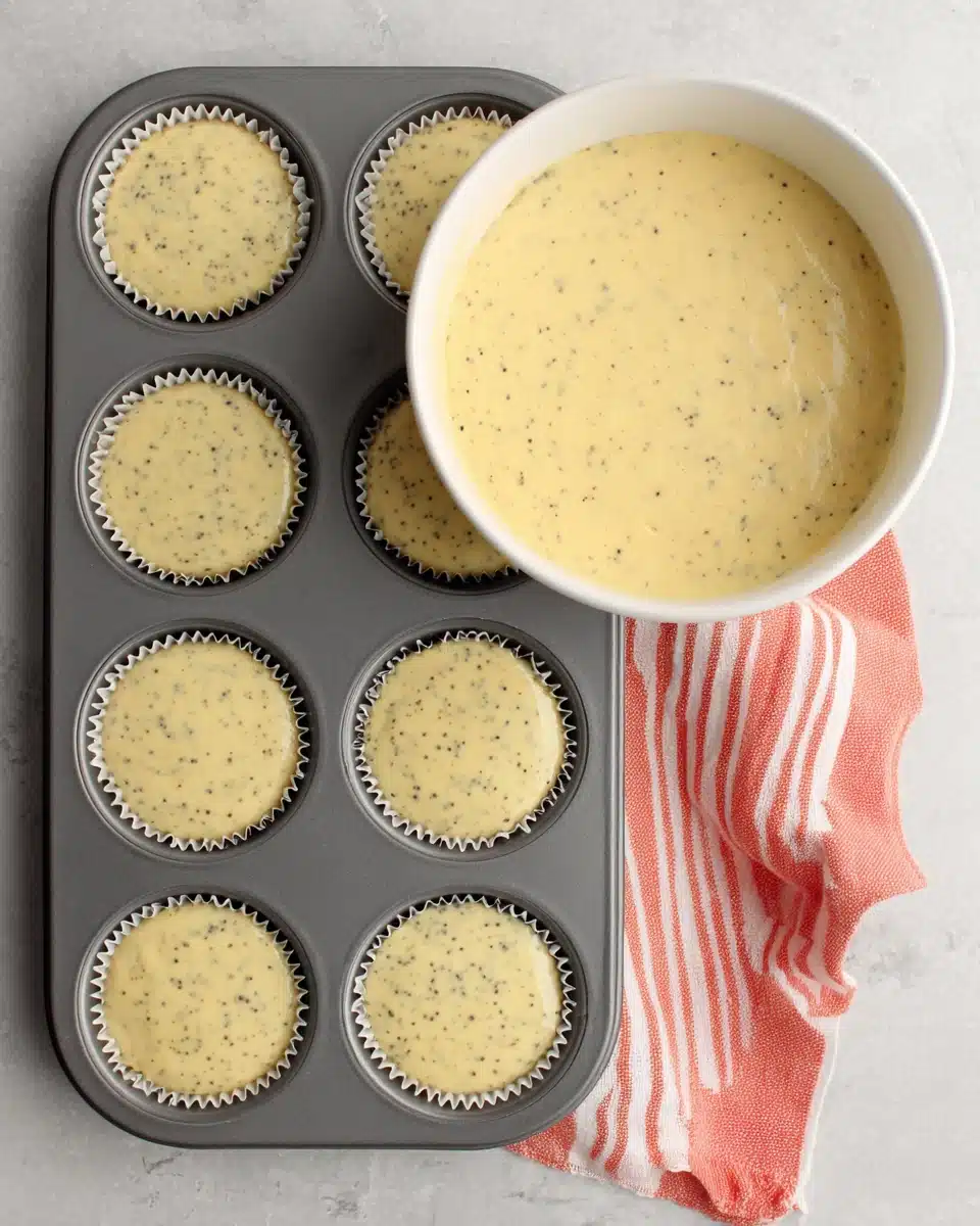 Lemon poppyseed cupcake batter in a bowl with filled liners.