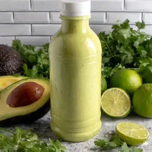 Avocado crema in a squeeze bottle with fresh avocados, limes, and cilantro