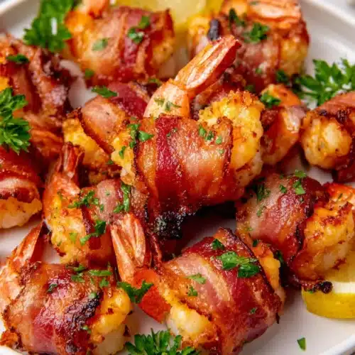 Crispy bacon wrapped shrimp on a plate with lemon garnish