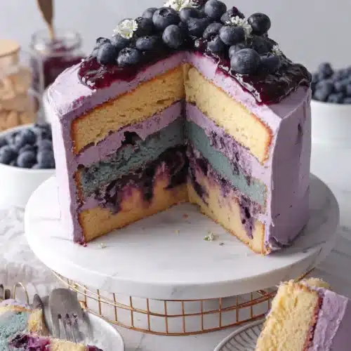 Blueberry layer cake with purple frosting and fresh blueberries, sliced to show layers