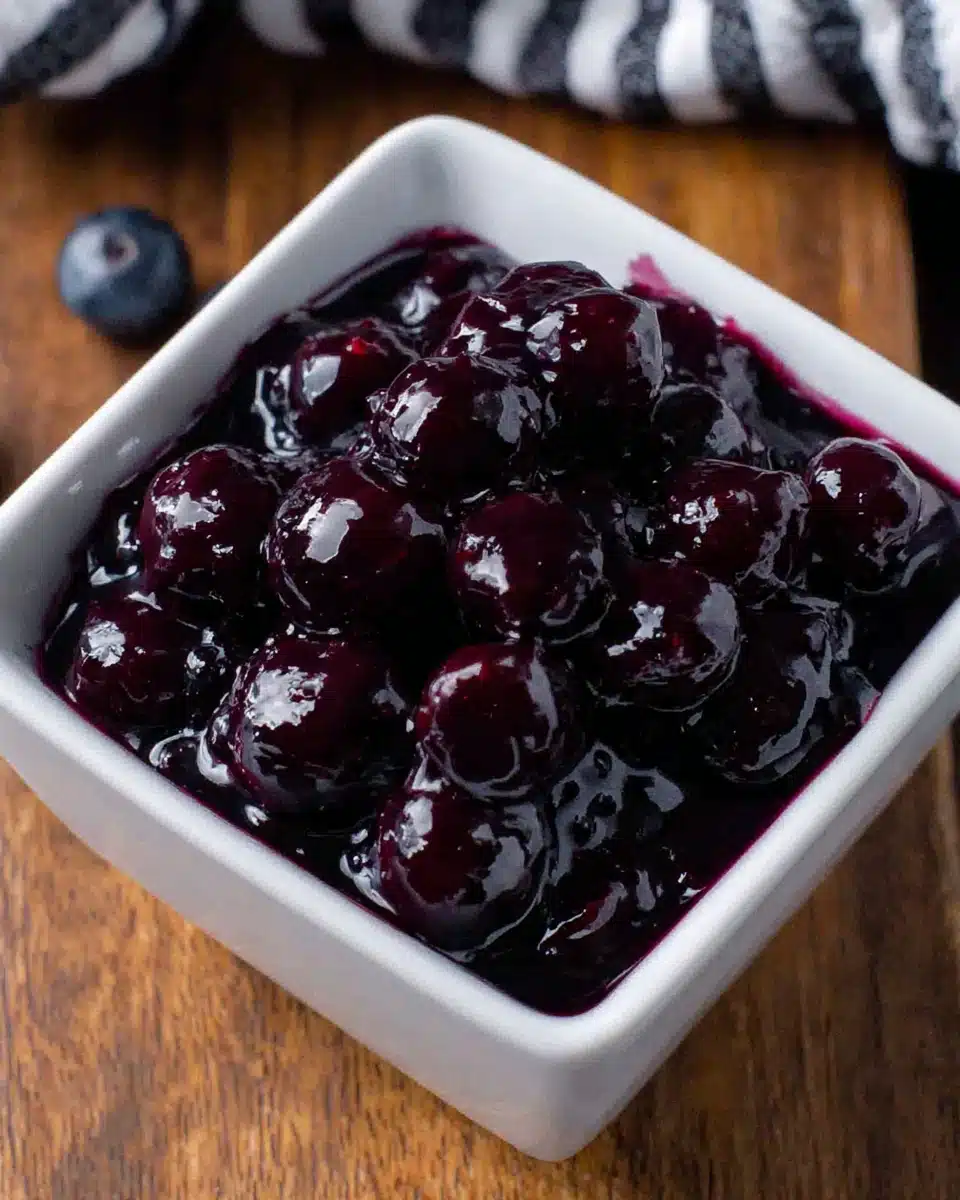 Glossy blueberry sauce in a white bowl on wooden surface