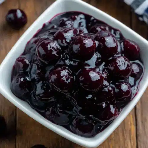 Glossy blueberry sauce in a white bowl on wooden surface