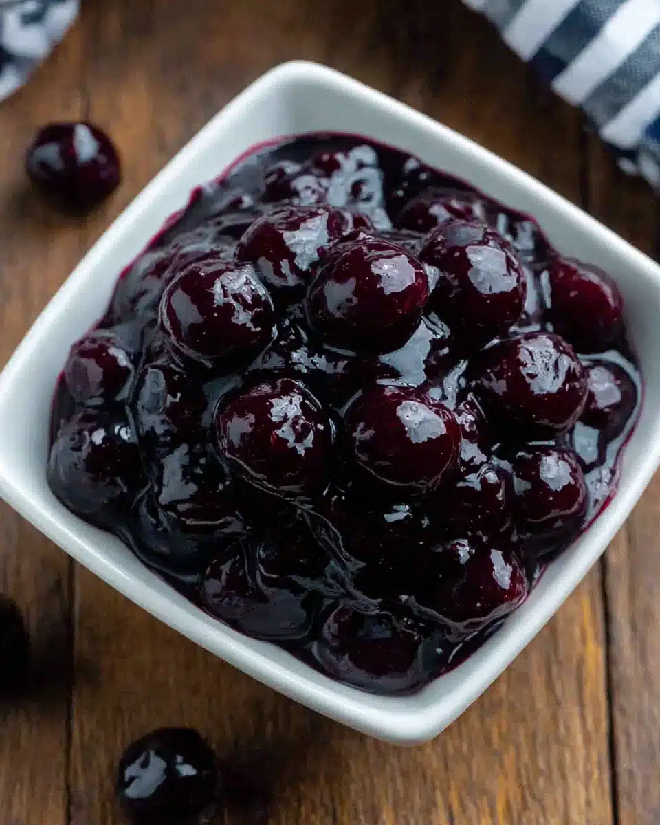 Glossy blueberry sauce in a white bowl on wooden surface
