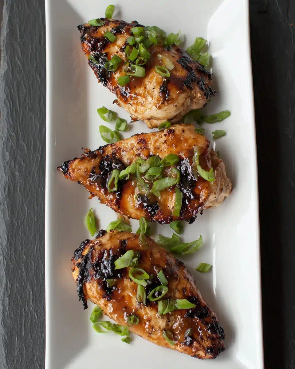 Juicy chicken breasts marinated and broiled, garnished with green onions on a white plate