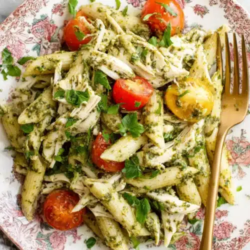 Chicken pesto pasta salad with penne, chicken, tomatoes, and pesto on a floral plate