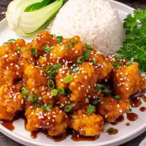 Crispy Chinese honey chicken with rice and vegetables, garnished with sesame seeds and green onions