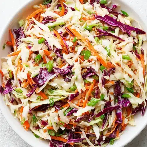 Coleslaw for pulled pork with green and red cabbage, carrots, and green onions in a white bowl