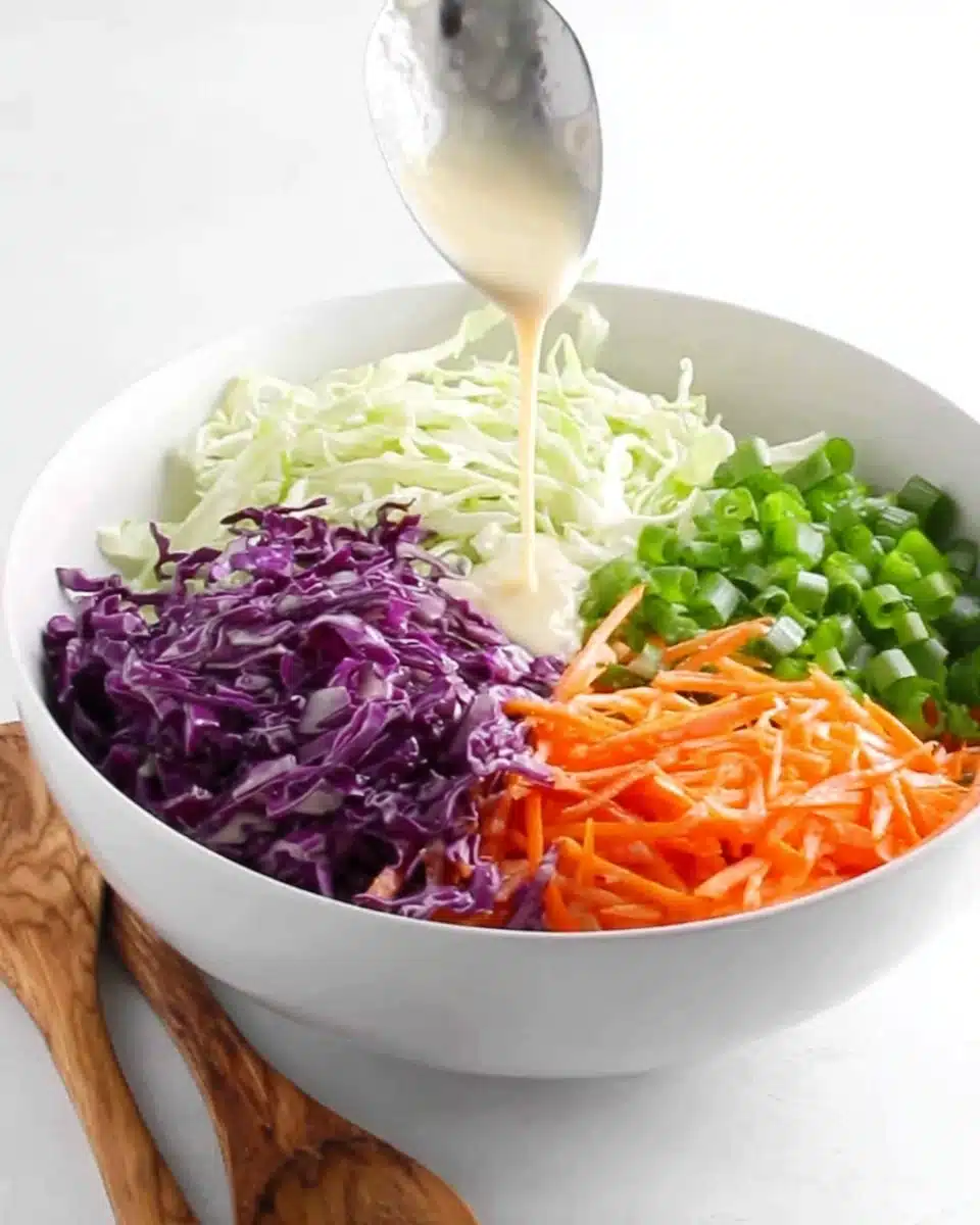 Coleslaw for pulled pork with shredded cabbage, carrots, green onions, and creamy dressing being poured.