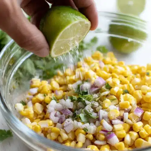 Hand squeezing lime over copycat Chipotle corn salsa with fresh corn, onions, and cilantro