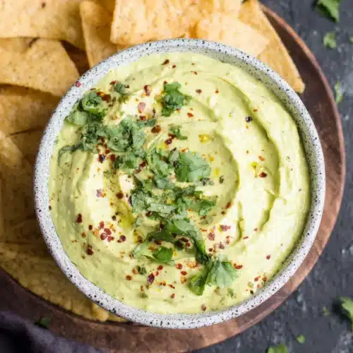 Creamy avocado dip with cilantro and tortilla chips on wooden tray