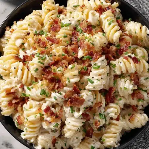 Creamy bacon cheddar ranch pasta salad with crispy bacon and green onions in a black bowl