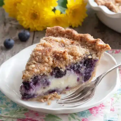 Creamy blueberry pie slice with streusel topping on a white plate