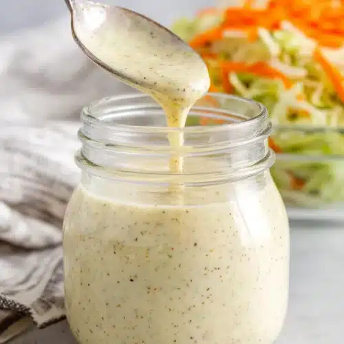 Best Creamy Coleslaw Salad Dressing You’ll Ever Make 1 Creamy coleslaw salad dressing in a jar with a spoon, fresh vegetables nearby