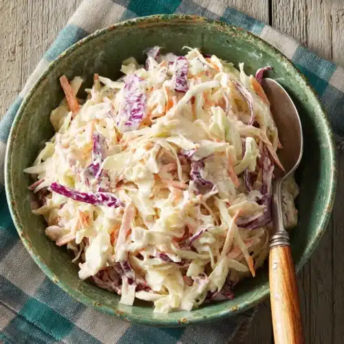 Easy Creamy Coleslaw Recipe for Delicious Gatherings 1 Creamy coleslaw with shredded cabbage and carrots in a green bowl on a checkered napkin.