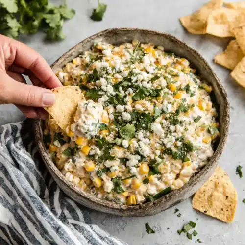 Creamy corn dip recipe with tortilla chips, cilantro, and Cotija cheese