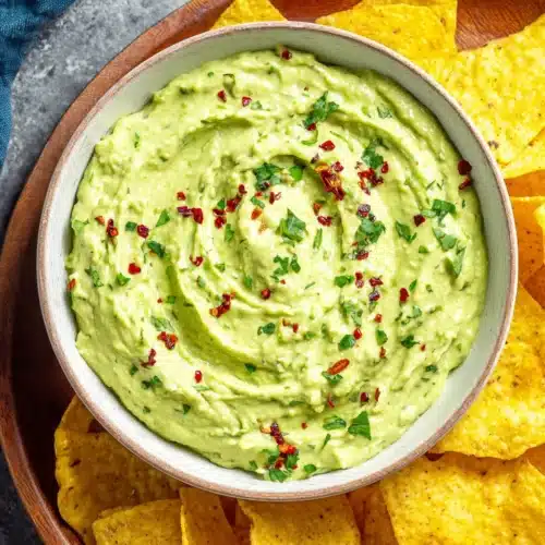 Creamy guasacaca in a white bowl with tortilla chips, garnished with herbs and chili flakes