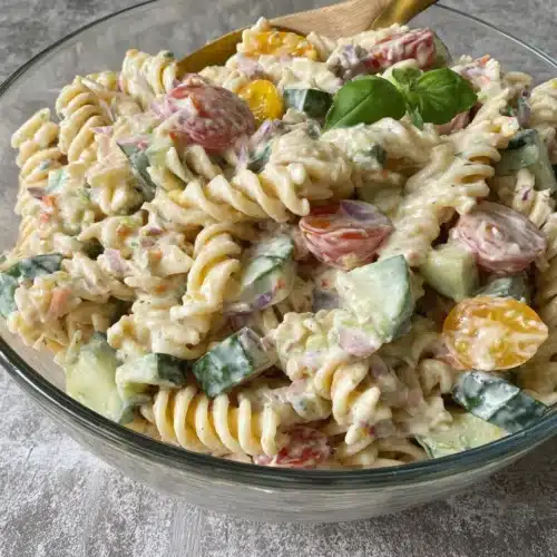 Creamy pasta salad with garden rotini, cucumbers, tomatoes, and bell peppers in a glass bowl