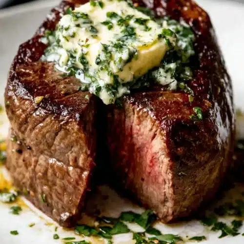 Filet mignon with garlic herb butter on a white plate, topped with melting herb butter