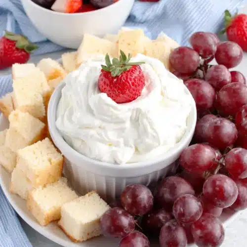 Creamy fruit dip served with strawberries, grapes, and pound cake on a white plate.