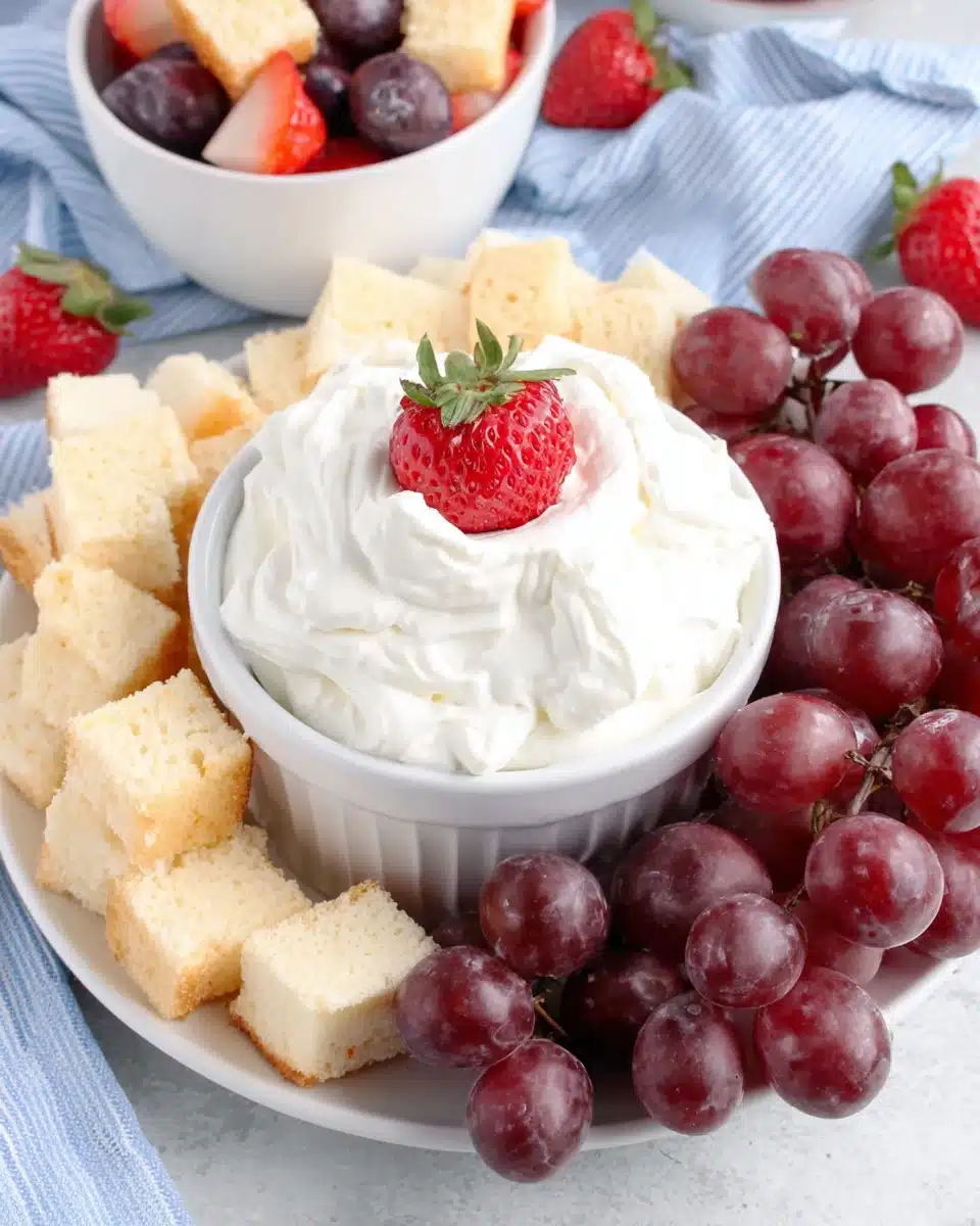 Creamy fruit dip served with strawberries, grapes, and pound cake on a white plate.