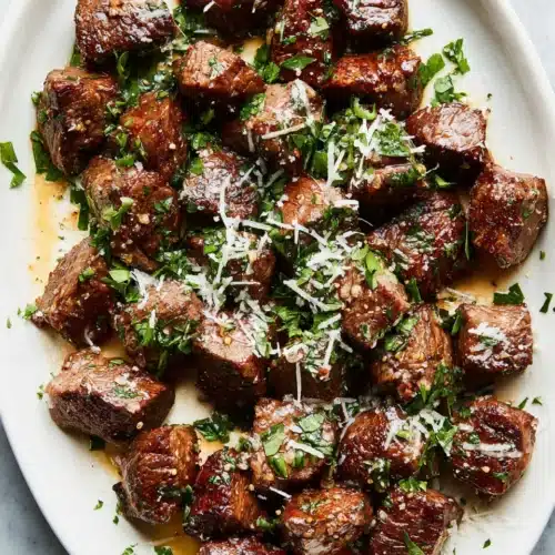 Garlic butter steak bites with parmesan, garnished with parsley on a white plate