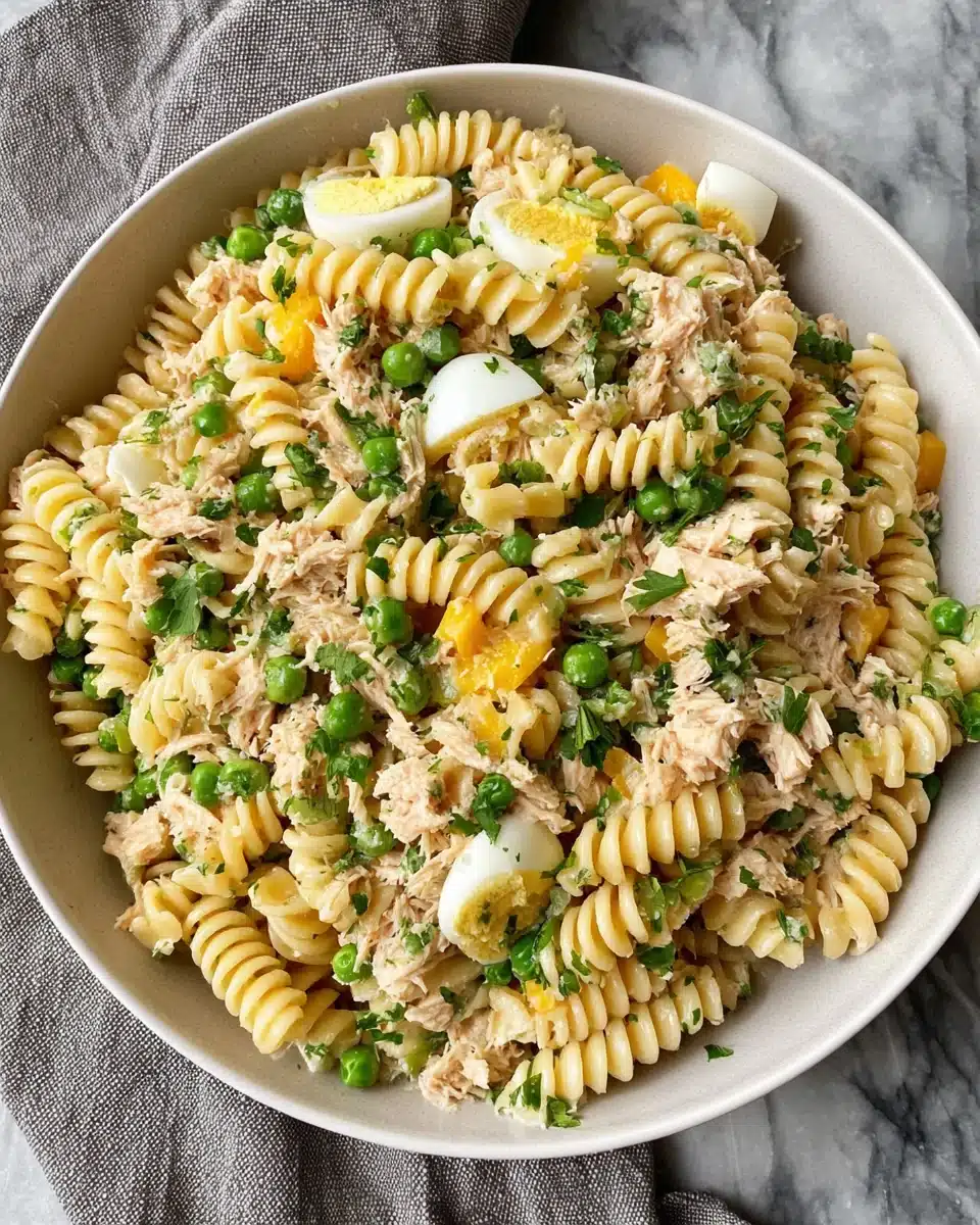 High protein tuna pasta salad with rotini, tuna, peas, and parsley in a white bowl