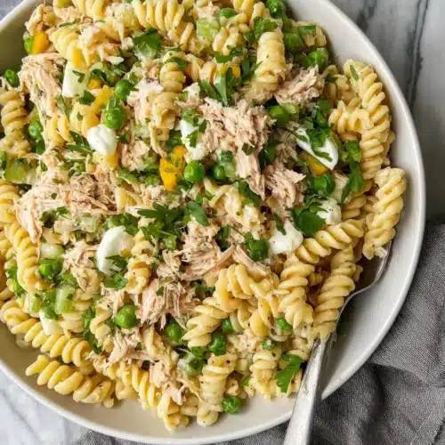 High protein tuna pasta salad with rotini, tuna, peas, and herbs in a white bowl