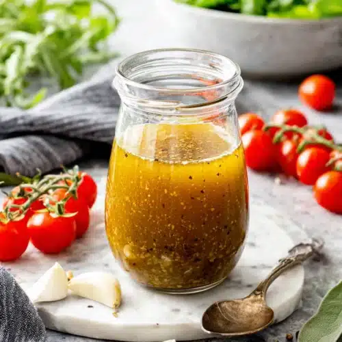 Italian chicken marinade in a glass jar with fresh herbs and tomatoes