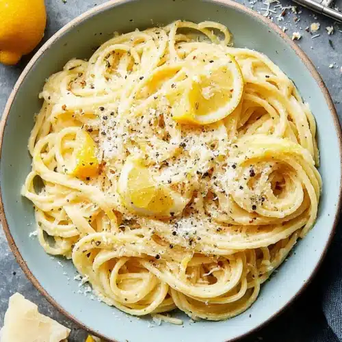 Lemon butter garlic pasta in a blue bowl with lemon slices and grated cheese