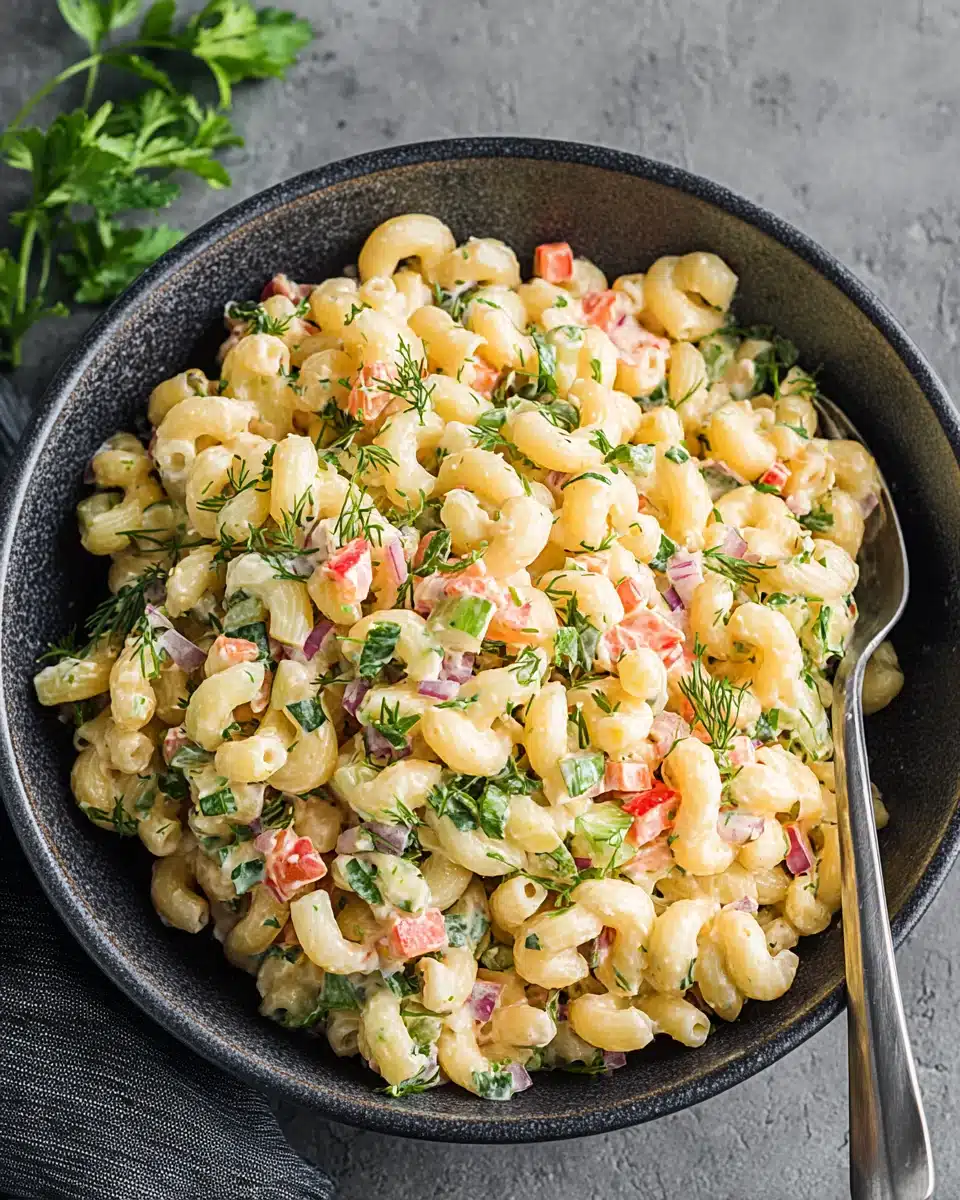 Creamy macaroni salad with vegetables and herbs in a dark bowl