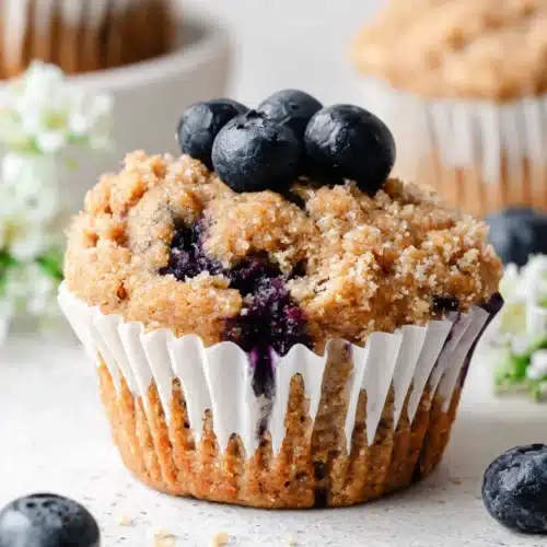 Mini blueberry banana muffin with fresh blueberries on top, in a white liner
