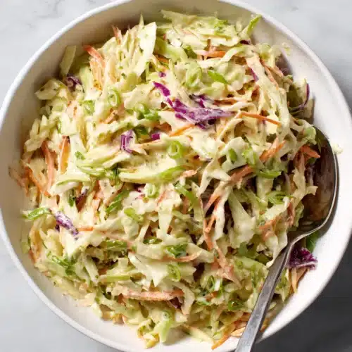 Creamy coleslaw with green and purple cabbage, carrots, and green onions in a white bowl