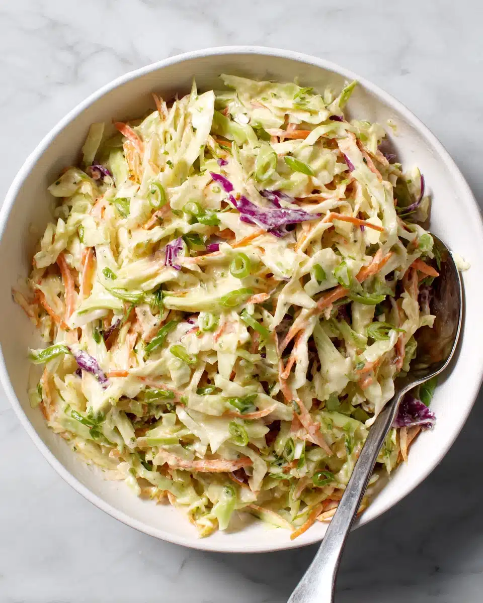 Creamy coleslaw with green and purple cabbage, carrots, and green onions in a white bowl