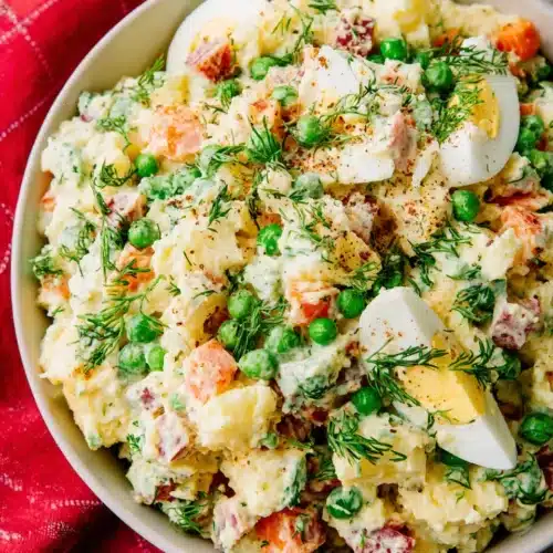 Olivier Russian potato salad with potatoes, peas, eggs, and dill in a white bowl