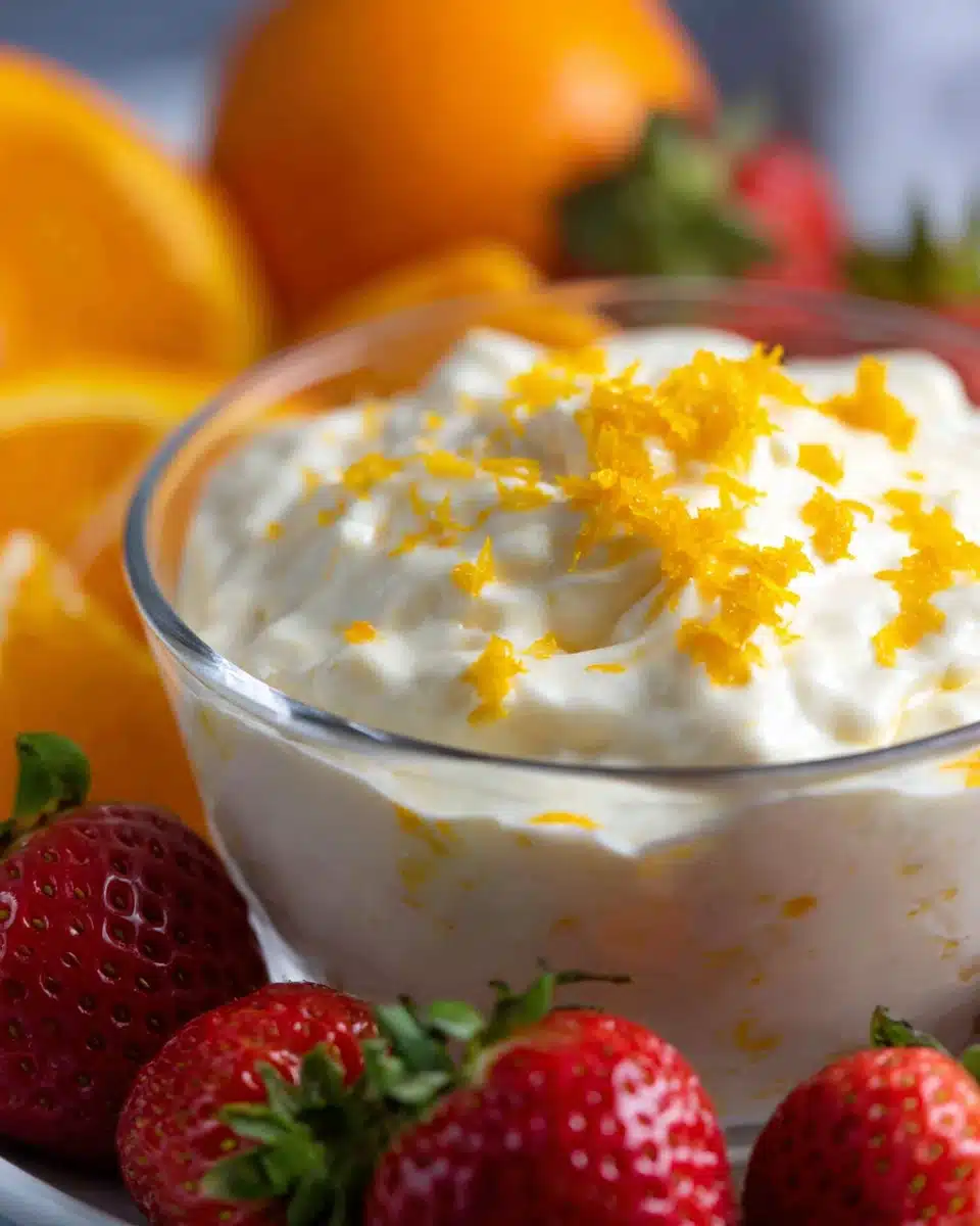 Orange creamsicle fruit dip in a glass bowl with strawberries and orange zest