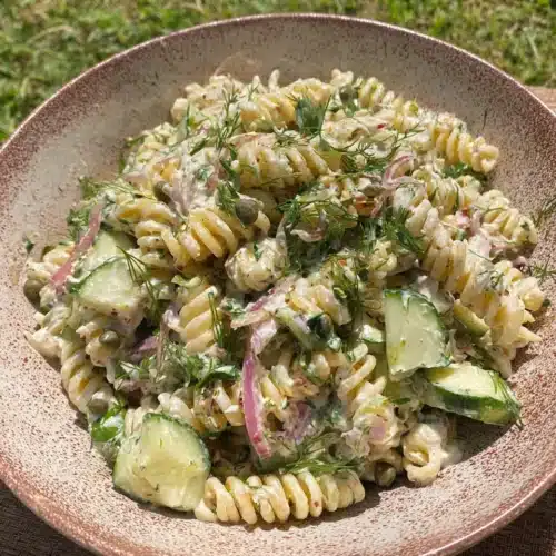 Pasta salad with goat cheese vinaigrette in a ceramic bowl, featuring rotini, cucumbers, herbs, and capers