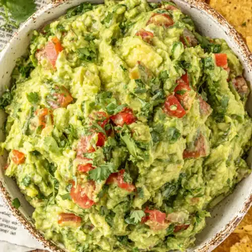 Simple & classic guacamole in a rustic bowl with tomatoes and cilantro