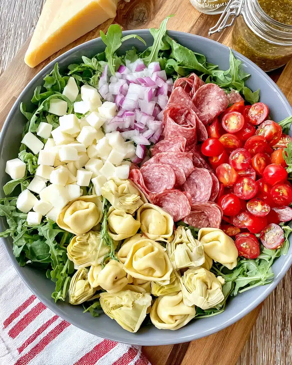 Tortellini Antipasto Salad with Fresh Greens and Meats Tortellini and antipasto salad with fresh greens, cheese, salami, tomatoes, and artichokes in a bowl