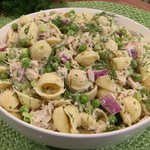 Creamy tuna noodle pasta salad with shell pasta, peas, and dill in a white bowl