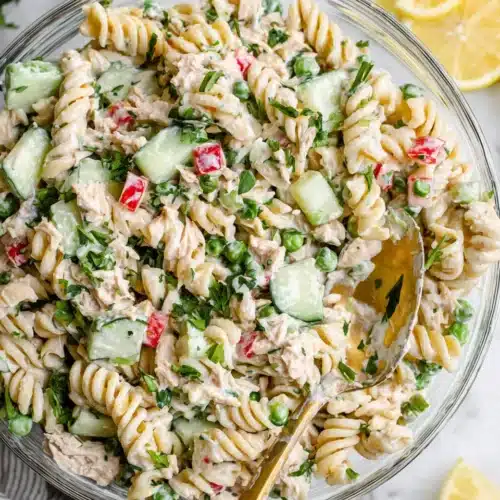 Super creamy tuna pasta salad with fresh veggies and herbs in a glass bowl