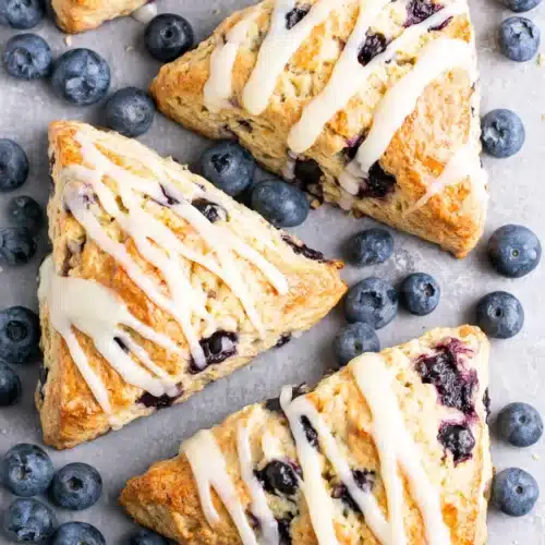 Vegan blueberry scones with white glaze and fresh blueberries on a baking sheet