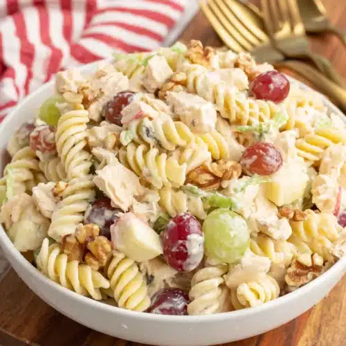 Waldorf chicken pasta salad with rotini, chicken, grapes, apples, and walnuts in a white bowl