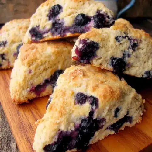 Golden whole wheat blueberry scones with fresh blueberries on wooden board