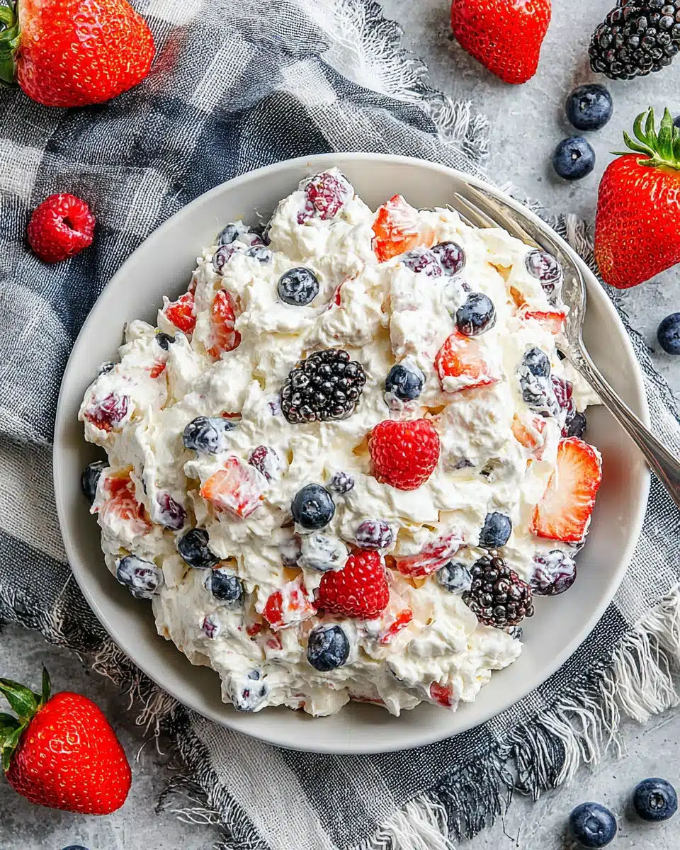 Berry cheesecake salad with fresh strawberries, blueberries, raspberries, and blackberries on a white plate.