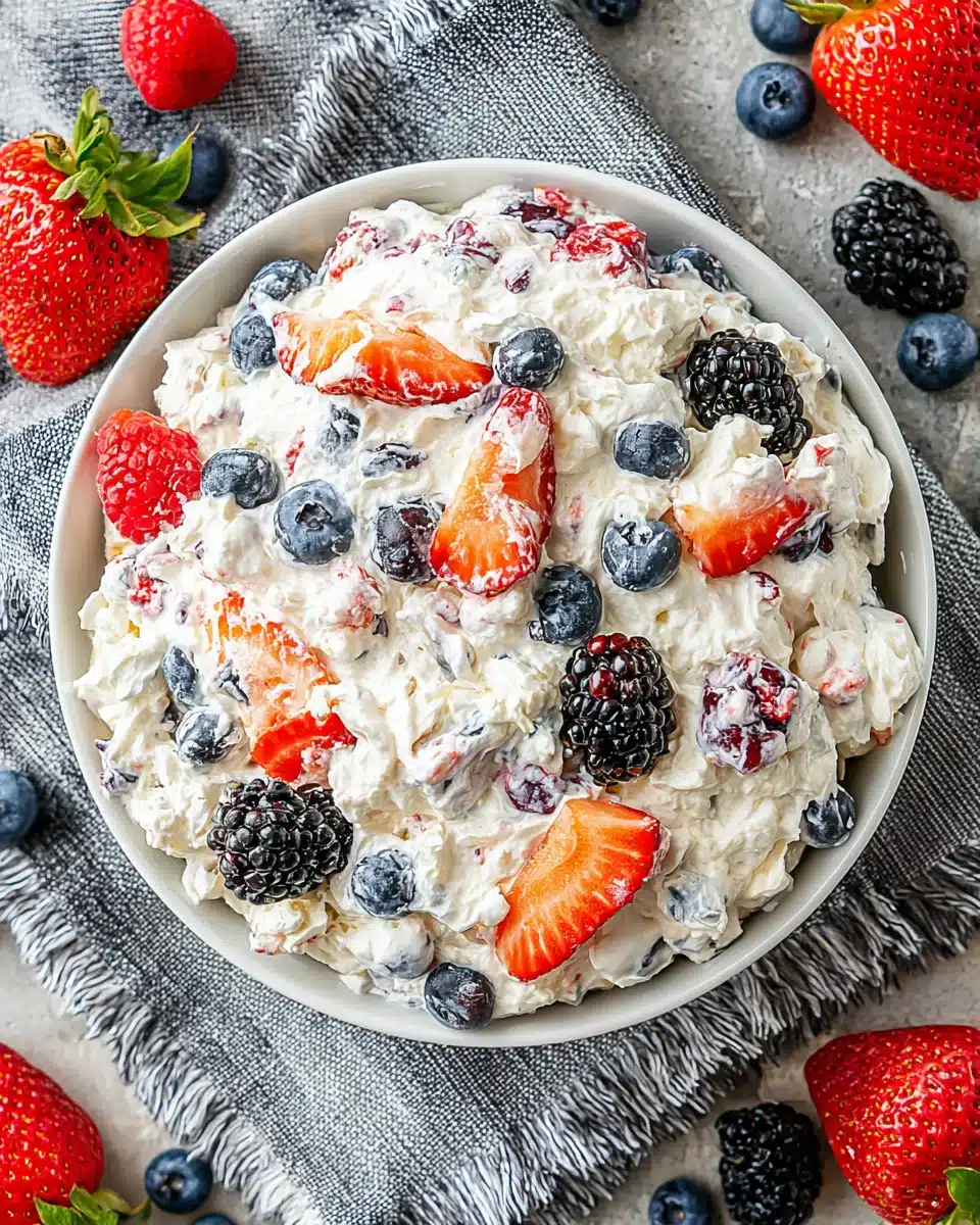 Berry cheesecake salad with fresh strawberries, blueberries, raspberries, and blackberries on a white plate.