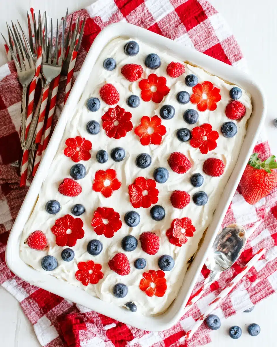 Berry tiramisu topped with fresh strawberries, raspberries, and blueberries on a checkered cloth