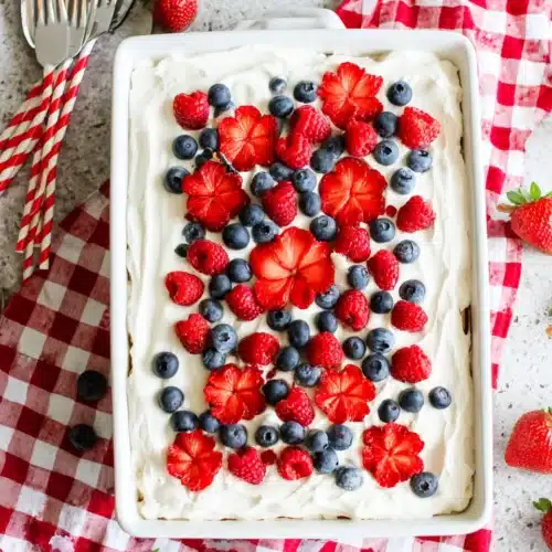 Berry tiramisu topped with fresh strawberries, raspberries, and blueberries on a checkered cloth