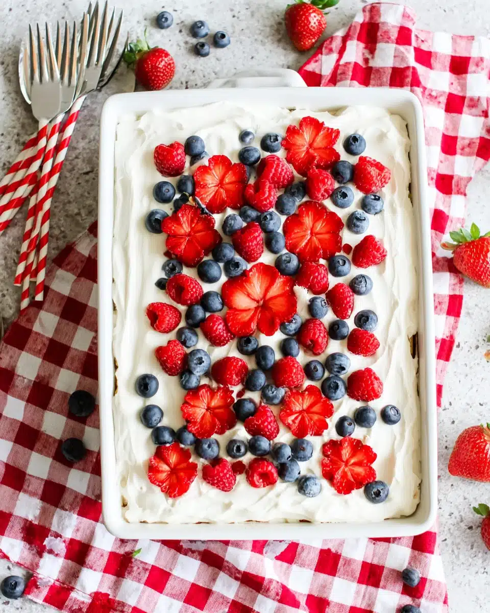 Berry tiramisu topped with fresh strawberries, raspberries, and blueberries on a checkered cloth